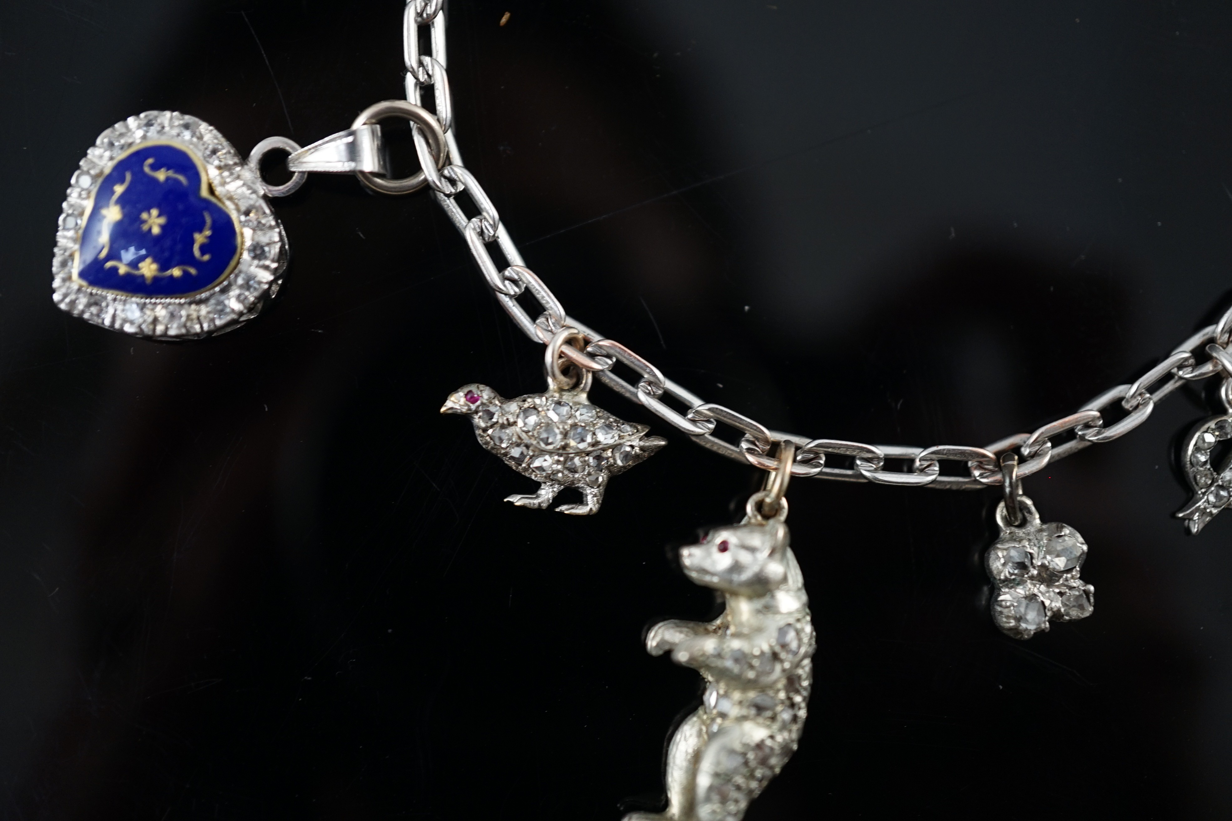 A 9ct white gold charm bracelet, with French platinum and diamond set clasp and hung with nine assorted charms, eight set with diamonds